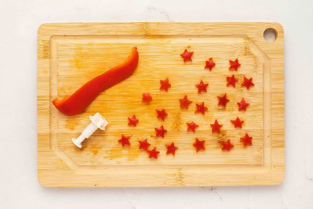Small red bell pepper stars cut out with a mini star cutter on a wooden cutting board.