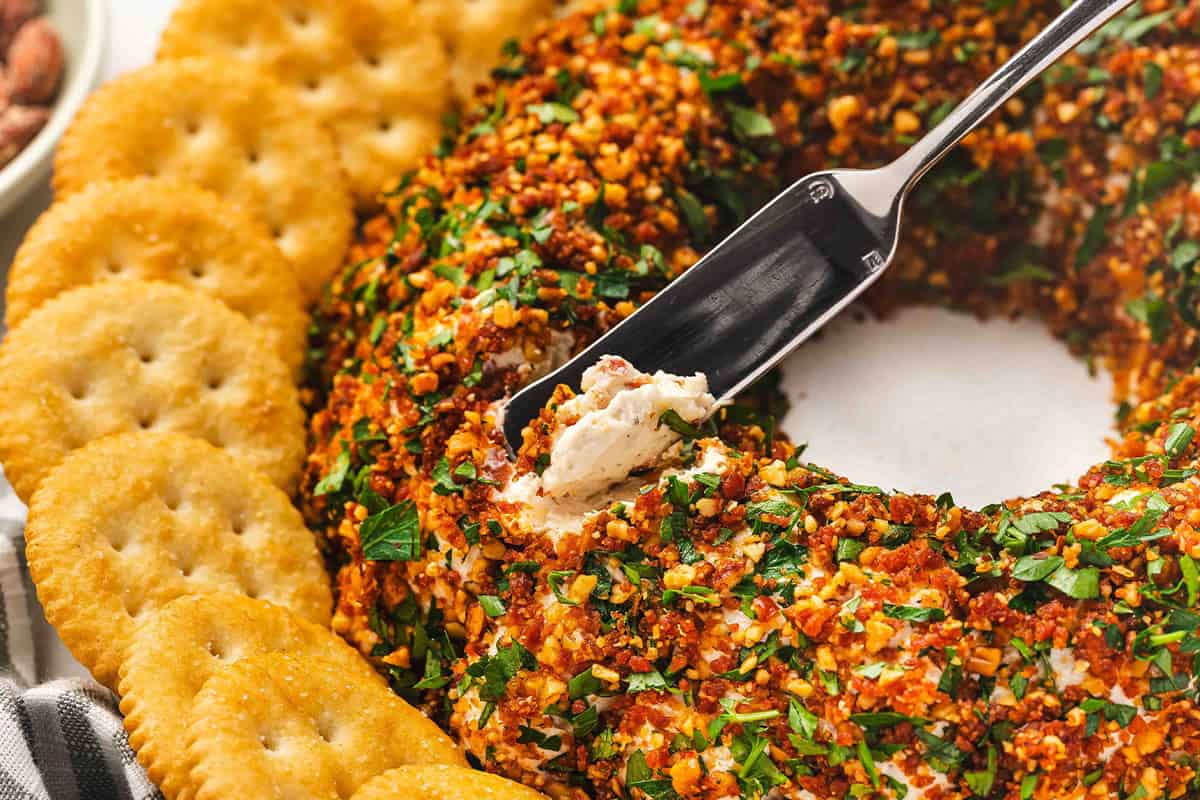 Close-up of a cheese spreader lifting a portion of the coated cheese ball onto a cracker.