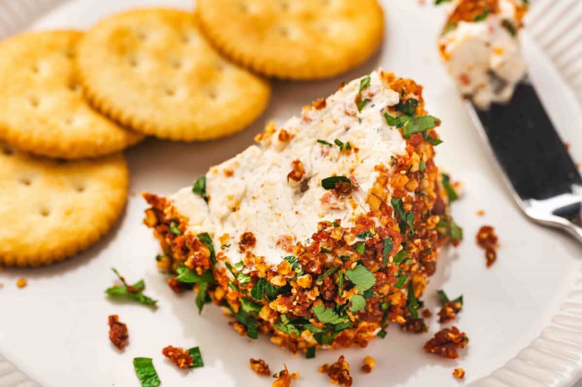 Slice of the Christmas wreath cheese ball served on a plate with round crackers on the side.
