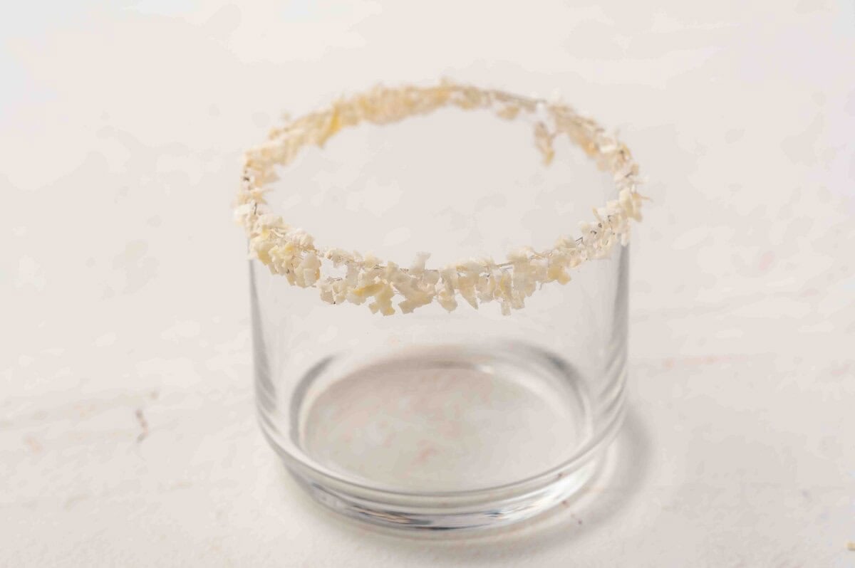 Close-up of a cocktail glass rim coated in coconut flakes for serving white Christmas punch.