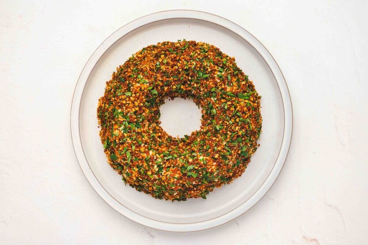 Cheese ball wreath fully coated with the almond, tomato, and parsley mixture on a serving plate.