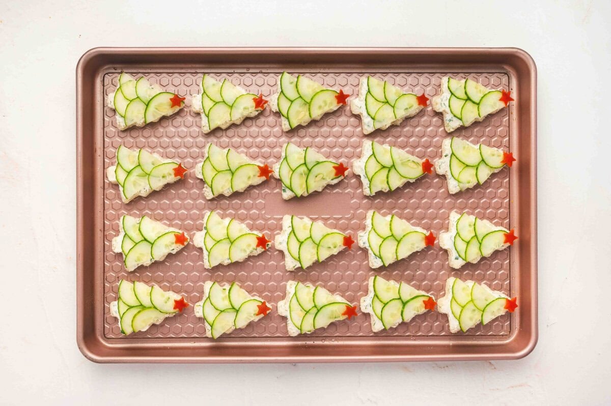 Rows of Christmas tree cucumber sandwiches arranged on a baking sheet, ready to serve.