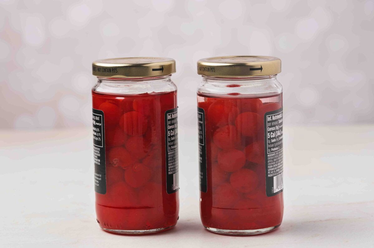 Two jars of maraschino cherries fully covered in vodka and sealed with gold lids.