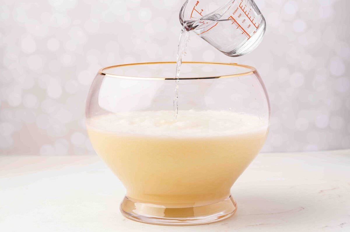 Pouring white cranberry and pineapple punch mixture into a large clear punch bowl.