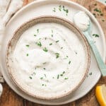 A bowl of creamy homemade horseradish sauce topped with chopped fresh chives, served on a plate with a spoon and lemon wedge.