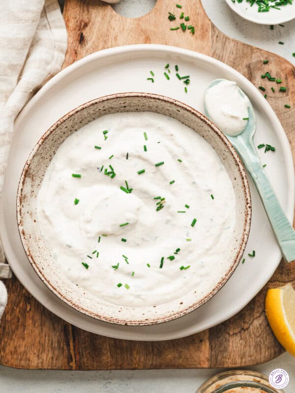 A bowl of creamy homemade horseradish sauce topped with chopped fresh chives, served on a plate with a spoon and lemon wedge.