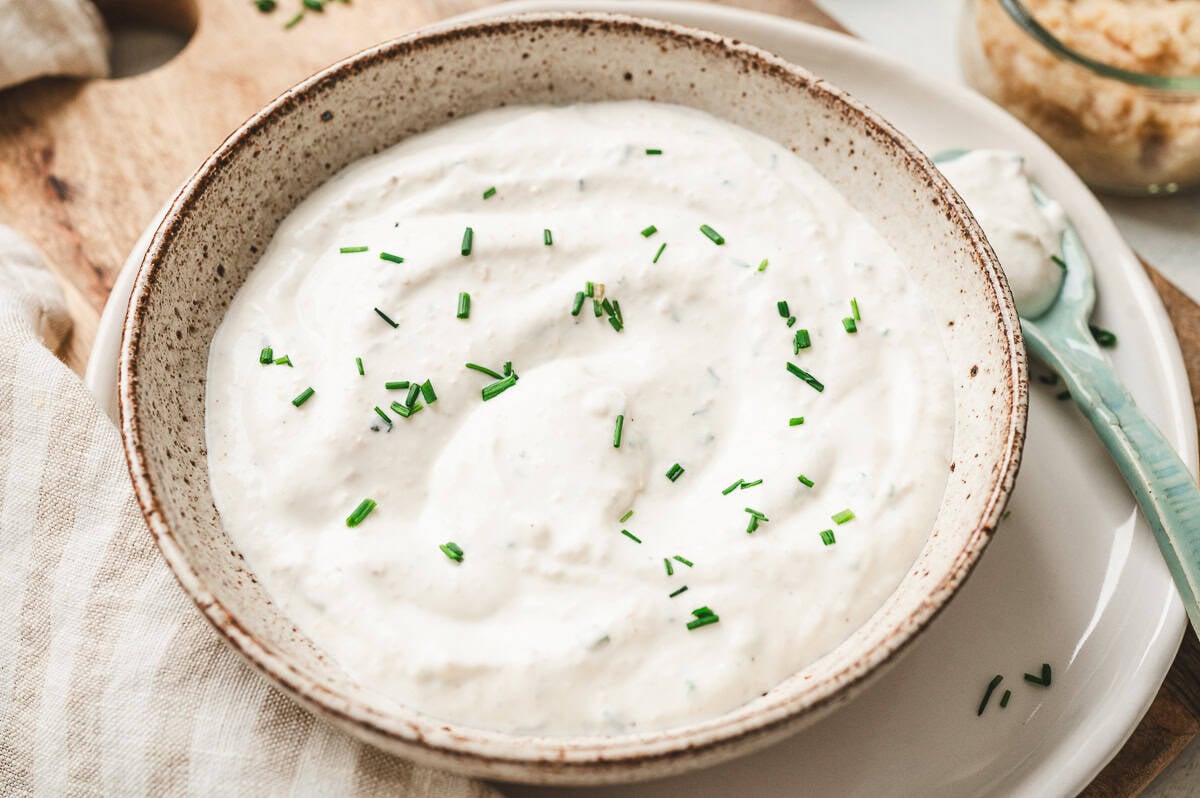 Close-up view of creamy horseradish sauce in a speckled bowl, garnished with chopped chives.