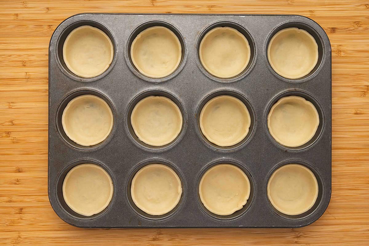 pie dough inserted into muffin tin slots for mini pies
