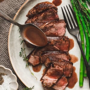 Sliced medium-rare steak on a plate with asparagus, topped with homemade red wine sauce being spooned over the meat.
