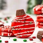 Red chocolate-covered Ritz cracker ornament cookie topped with a mini Reese’s cup, drizzled with white chocolate and holiday sprinkles.