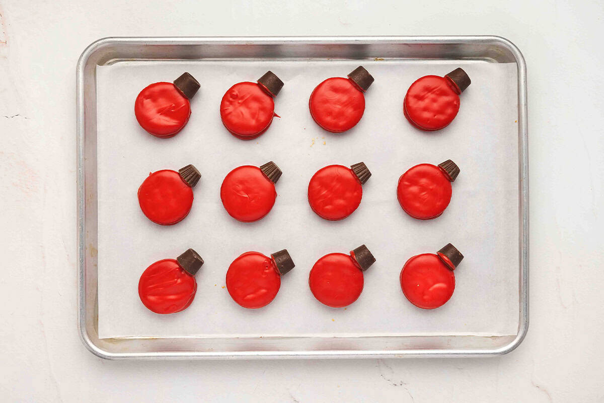Red-dipped Ritz cookies on a baking sheet with Rolos attached on top to look like Christmas ornament hooks.