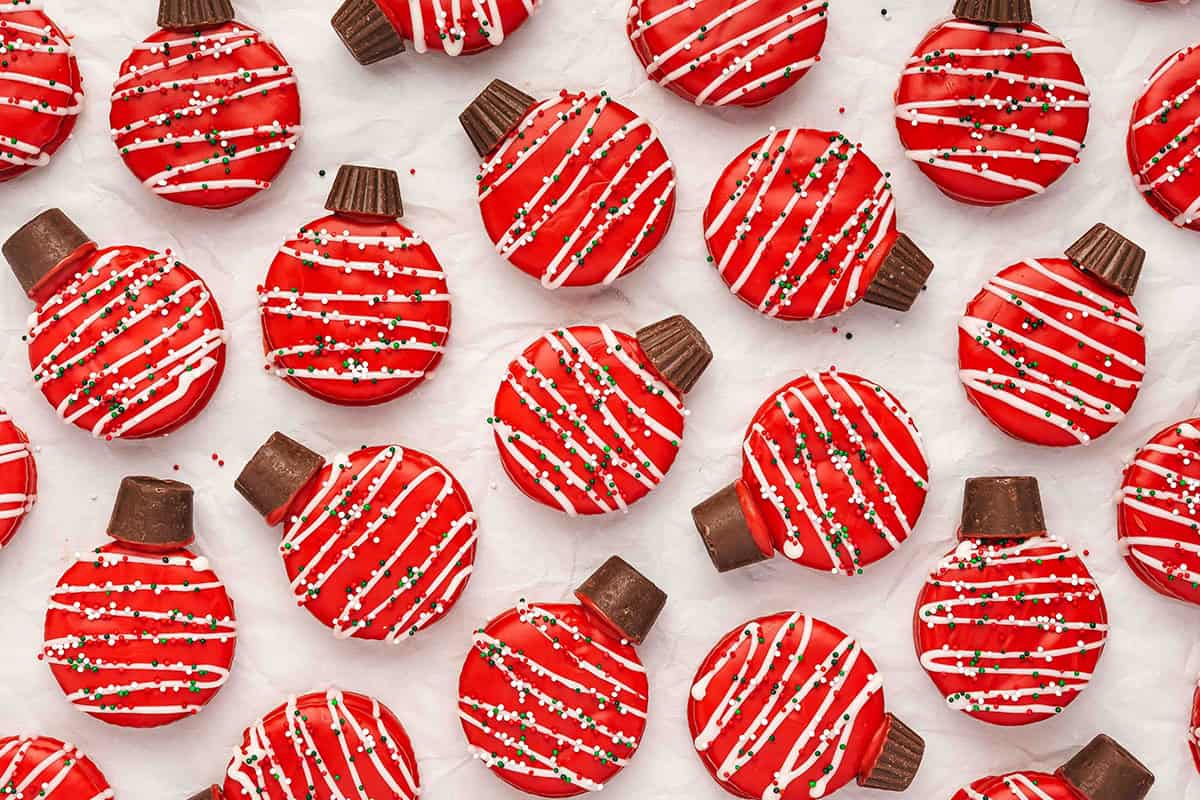 Assorted red chocolate-covered Ritz cracker ornament cookies drizzled with white chocolate and sprinkles, arranged on parchment.