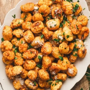 Golden, crispy air fryer gnocchi on a platter, topped with grated Parmesan and fresh parsley.