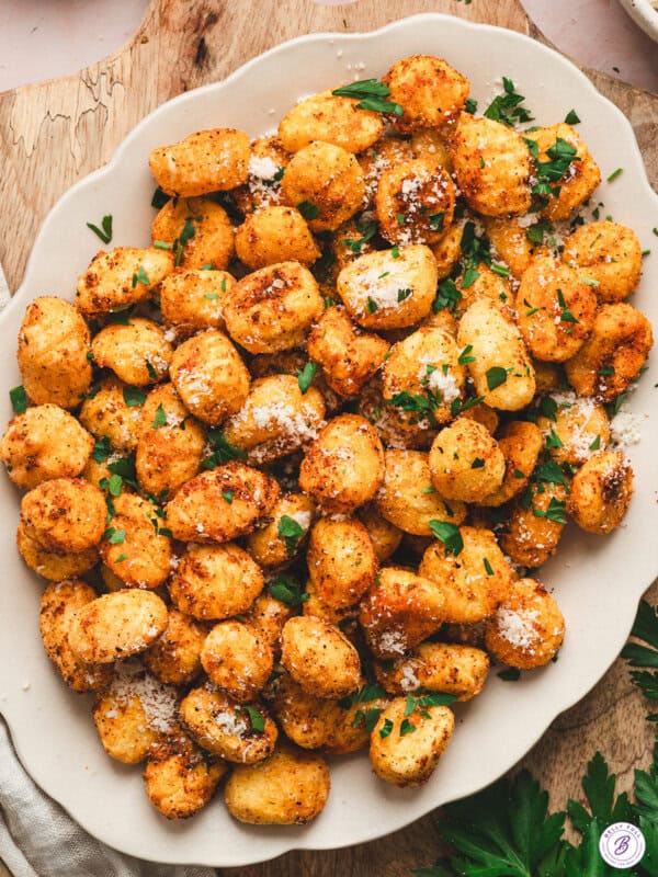 Golden, crispy air fryer gnocchi on a platter, topped with grated Parmesan and fresh parsley.