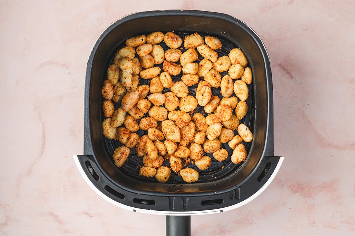 Seasoned gnocchi spread in a single layer inside the air fryer basket, ready to cook.