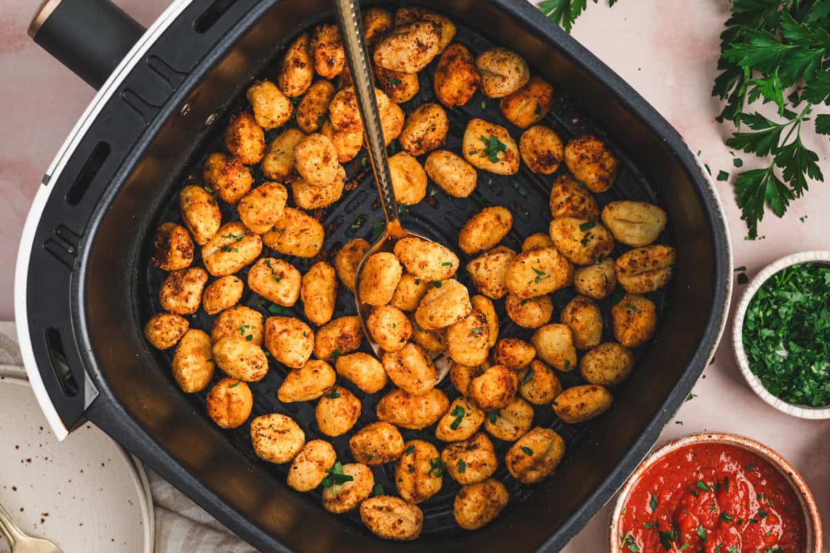 Crispy air-fried gnocchi in the air fryer basket with a spoon scooping some out, garnished with parsley.