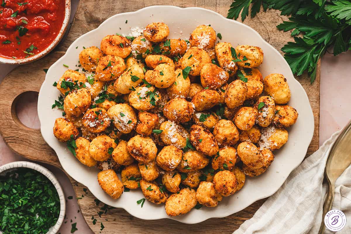 Air fryer gnocchi arranged on a platter with Parmesan and parsley, served with a bowl of marinara sauce on the side.