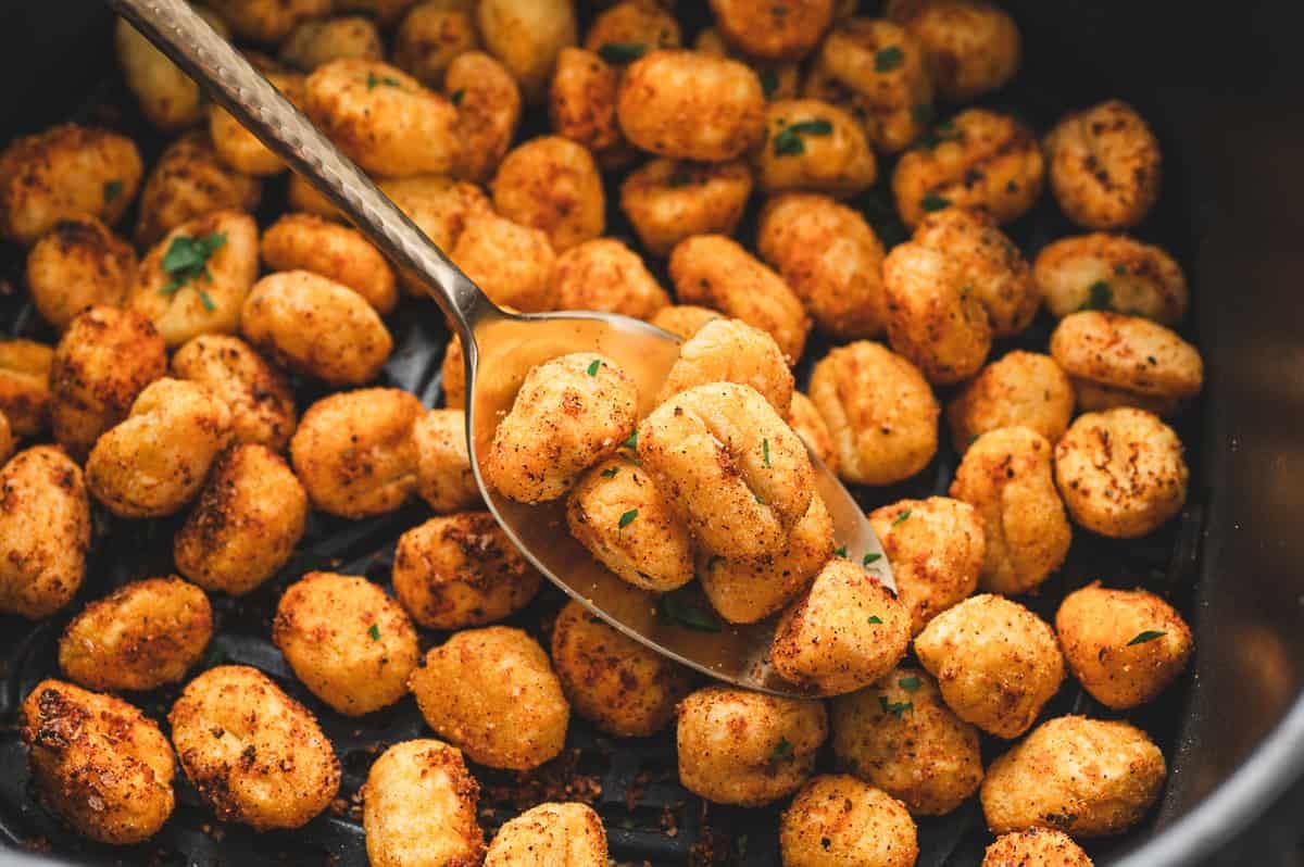 Close-up spoonful of crispy, golden gnocchi inside the air fryer basket, showing texture and seasoning.