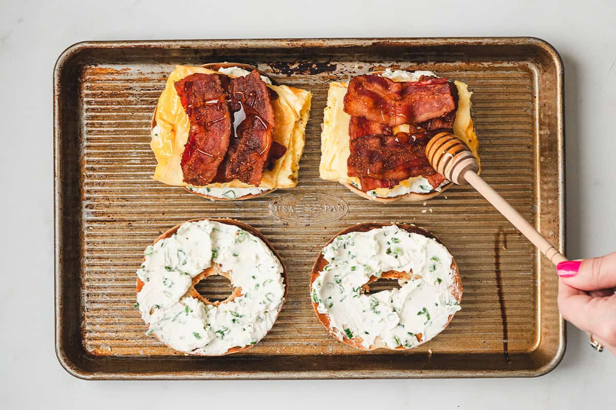 Drizzling hot honey over bacon and eggs on an open-faced bee sting bagel