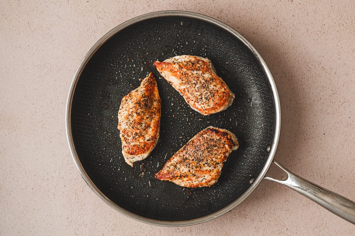 Seasoned chicken breasts searing in a skillet until golden brown