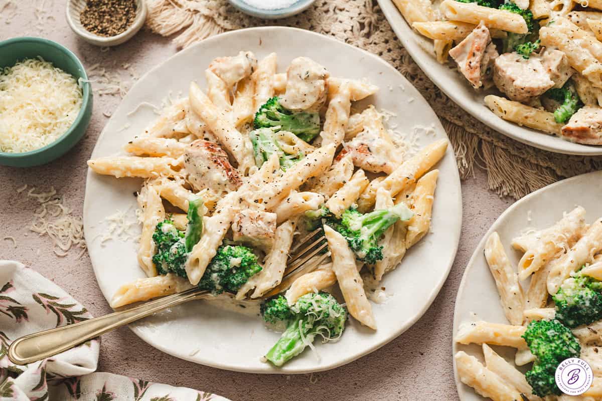Plates of chicken broccoli alfredo garnished with Parmesan and black pepper, ready to serve.