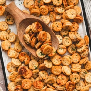 Sheet pan covered in baked Garlic Bread Ritz Bits with parsley, wooden scoop filled with crackers on top
