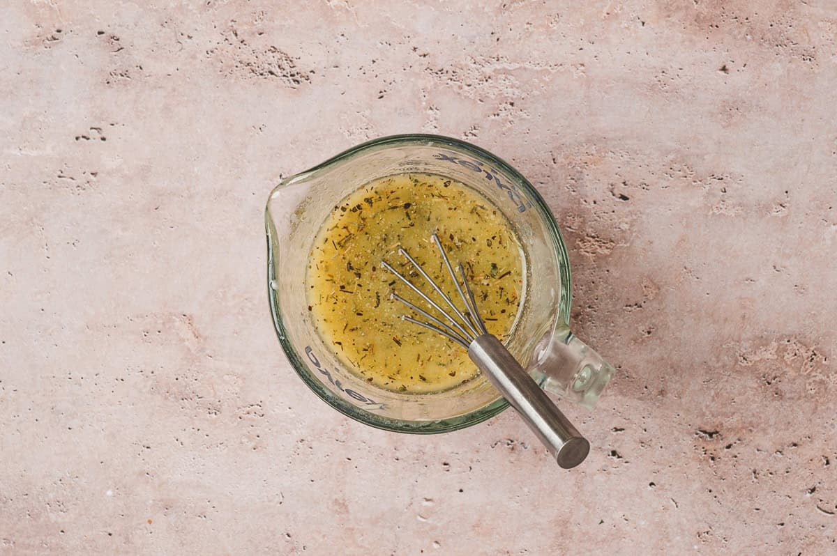 Measuring cup filled with melted butter, garlic powder, Italian seasoning, and onion powder mixture with a whisk inside