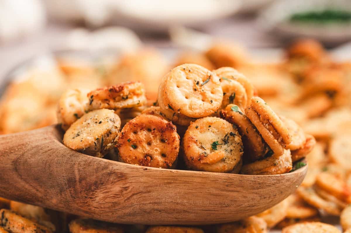 Wooden scoop filled with golden garlic Parmesan Ritz Bits with more crackers blurred behind