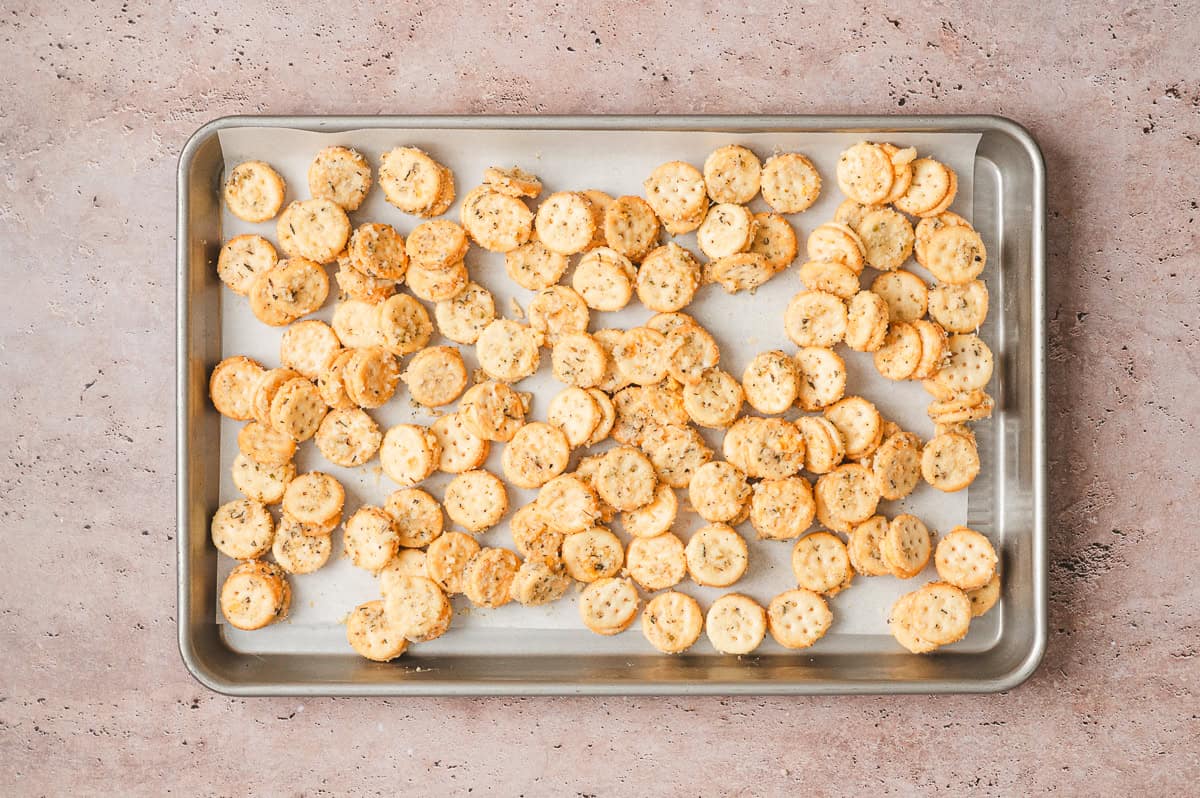 Seasoned Ritz Bits spread in a single layer on a parchment lined baking sheet before baking