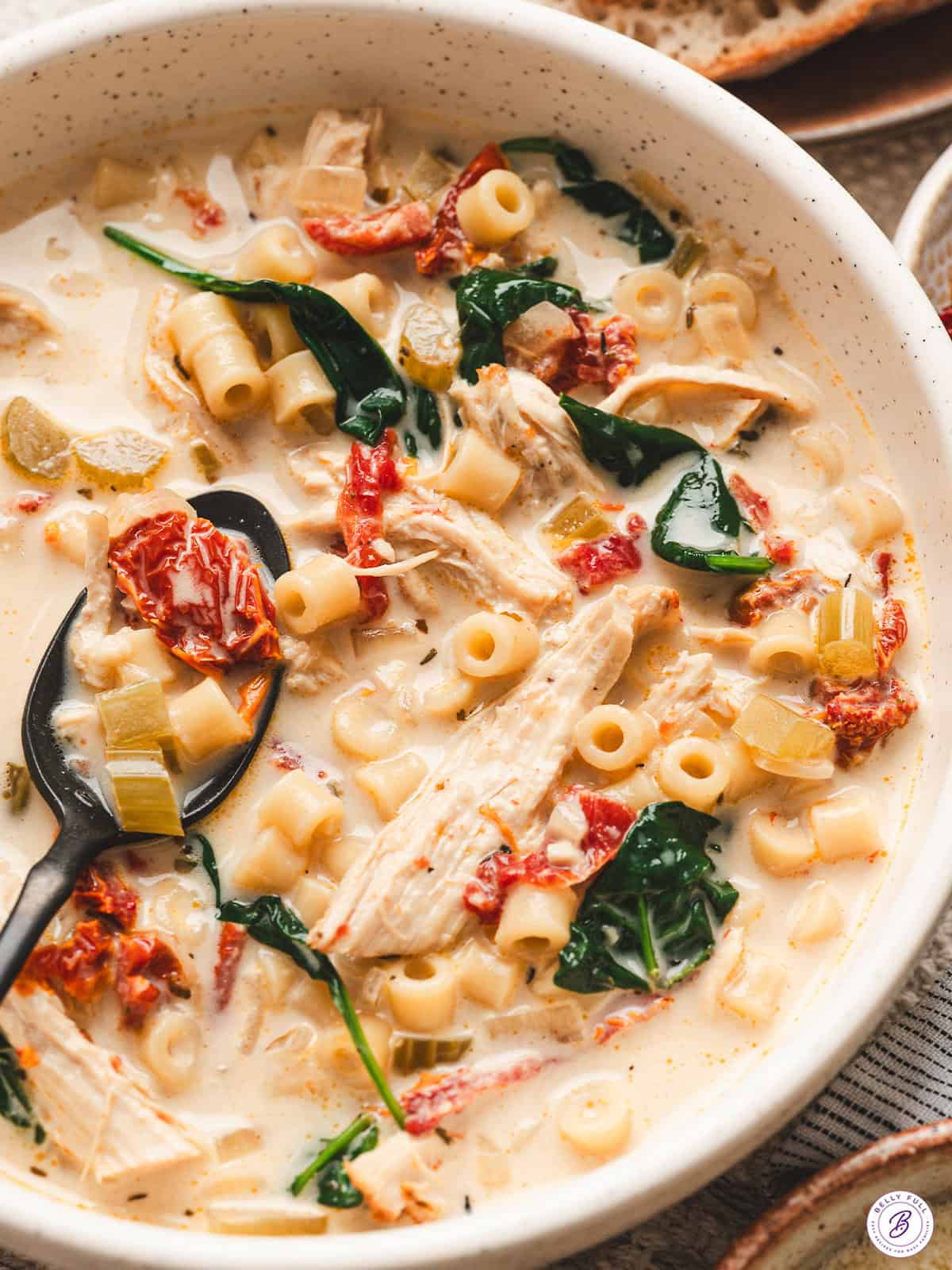 Creamy Marry Me Chicken Soup in a speckled bowl with ditalini pasta, shredded chicken, spinach, and sun dried tomatoes, served with bread on the side.