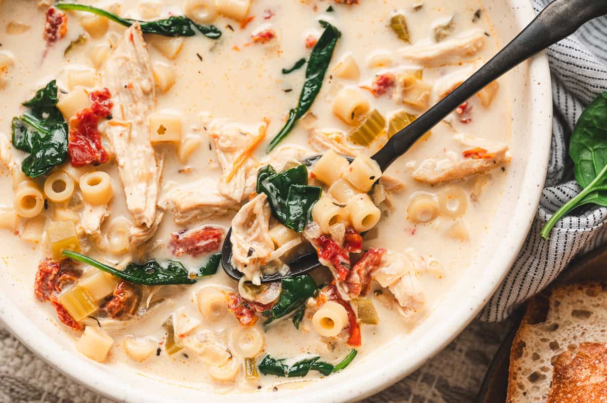 Close up bowl of Marry Me Chicken Soup with ditalini pasta, shredded chicken, spinach, and sun dried tomatoes, with a spoon lifting a hearty bite.