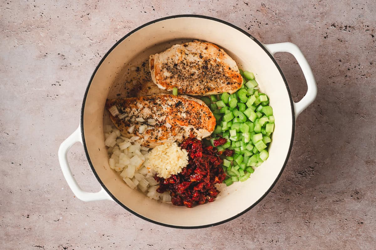 Browned chicken in a pot with diced onions, celery, garlic, and chopped sun dried tomatoes before cooking.