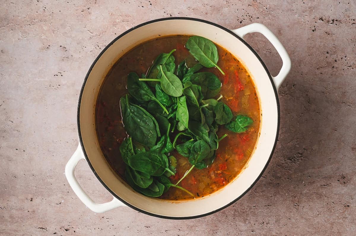 Fresh baby spinach added to simmering soup in a Dutch oven before stirring.