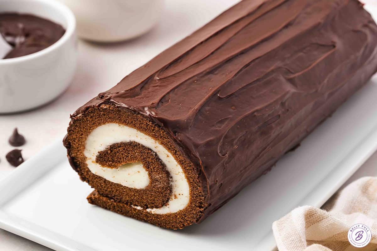 This easy Chocolate Swiss Roll Cake has a light sponge, creamy filling, and coated with a silky ganache. Chocolate Swiss Roll with end cut on serving tray