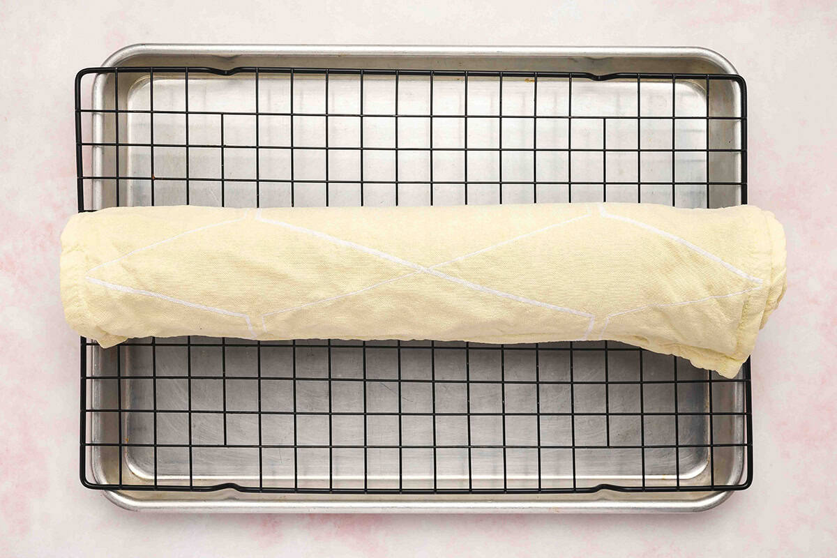 cake rolled in tea towel resting over baking rack