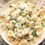 Creamy tortellini alfredo with peas, grated parmesan, and black pepper served in a white bowl