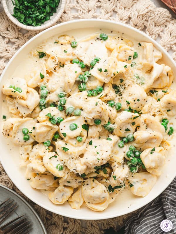 Creamy tortellini alfredo with peas, grated parmesan, and black pepper served in a white bowl