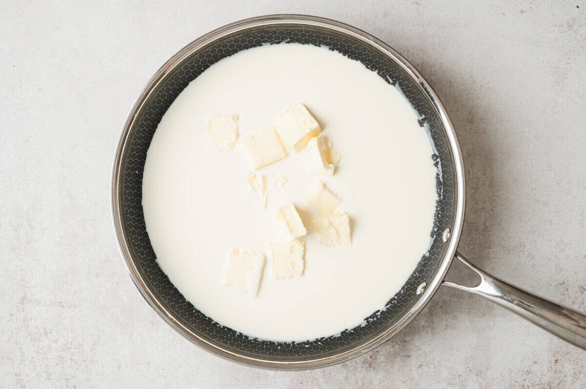 Butter cubes melting into heavy cream in a skillet to start homemade alfredo sauce
