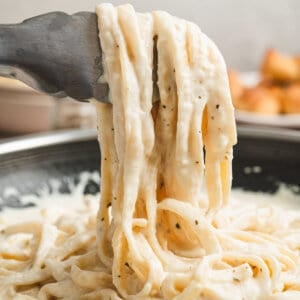 Alfredo sauce clinging to noodles hanging off of serving tongs