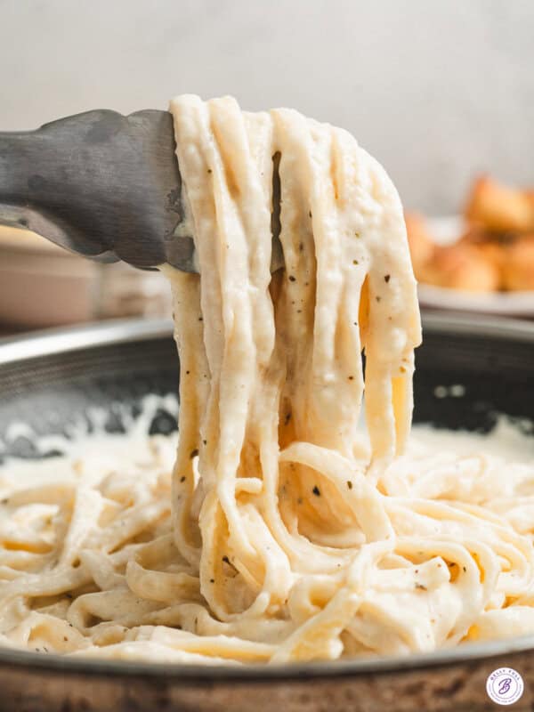 Alfredo sauce clinging to noodles hanging off of serving tongs