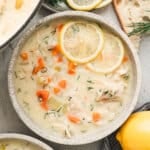 Creamy avgolemono soup with shredded chicken, rice, carrots, and dill, topped with lemon slices and served with crusty bread.