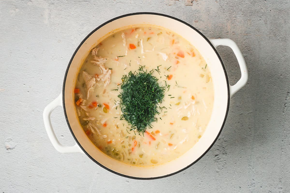 Avgolemono soup finished with fresh dill stirred in, showing a silky, creamy texture.