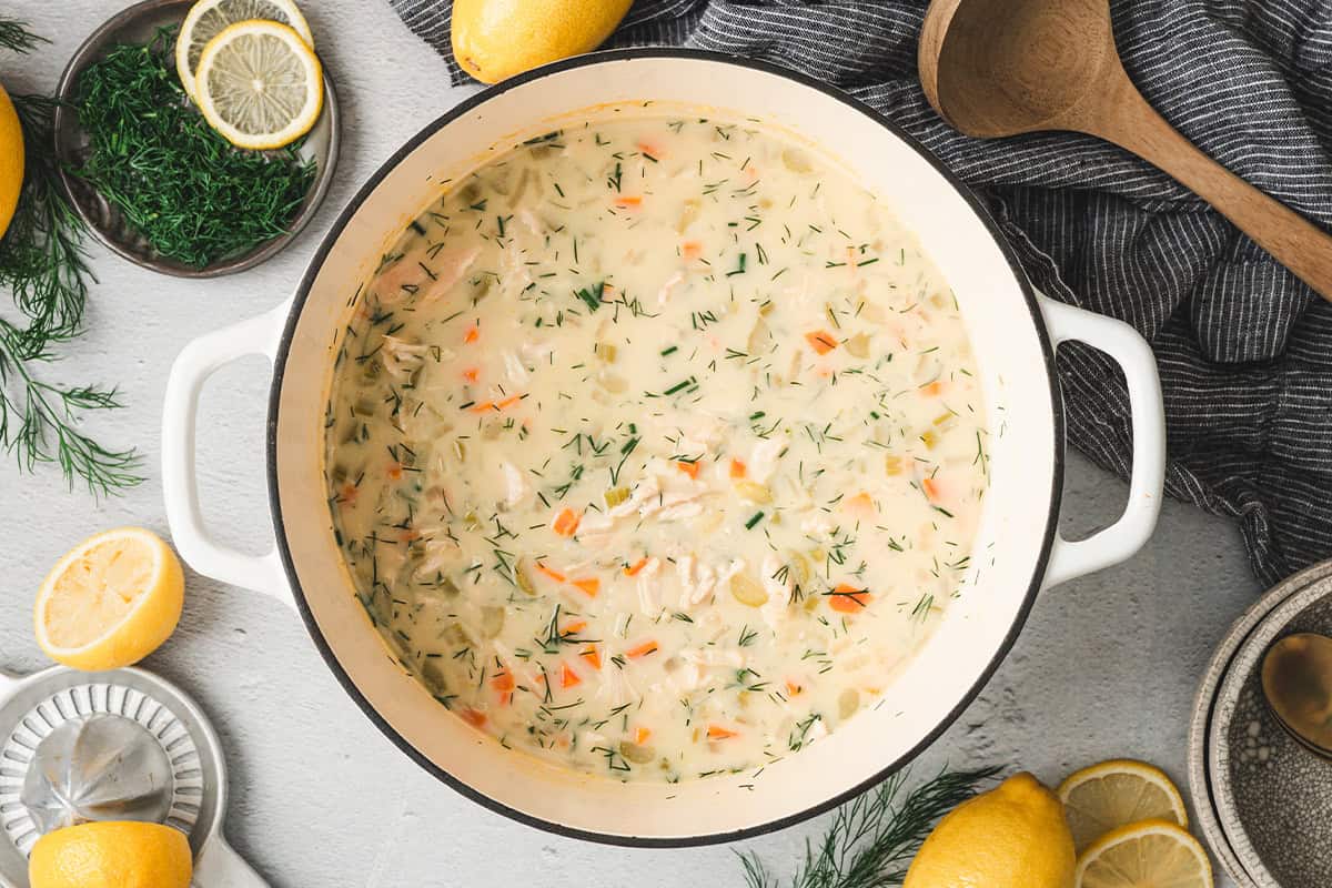 Large pot of Greek lemon chicken soup garnished with fresh dill, lemon halves, and served family-style.