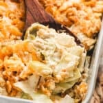 A wooden spoon scooping creamy cabbage casserole out of a baking dish.
