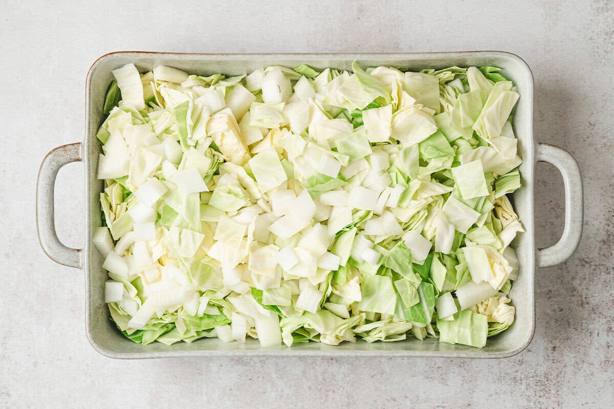 Chopped cabbage and onion in a baking dish.