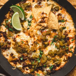 Baked chile relleno dip with melted cheese, roasted green chiles, and chorizo served in a cast iron skillet with tortilla chips and lime wedges.