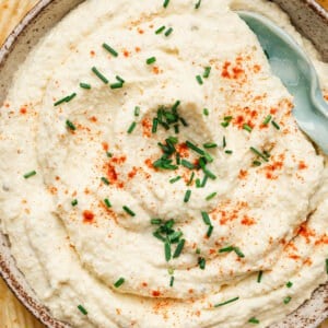 Creamy deviled egg dip garnished with paprika and chopped chives, served in a bowl surrounded by ridged potato chips.