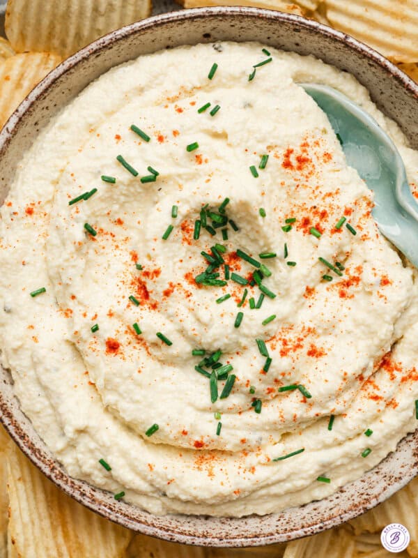 Creamy deviled egg dip garnished with paprika and chopped chives, served in a bowl surrounded by ridged potato chips.