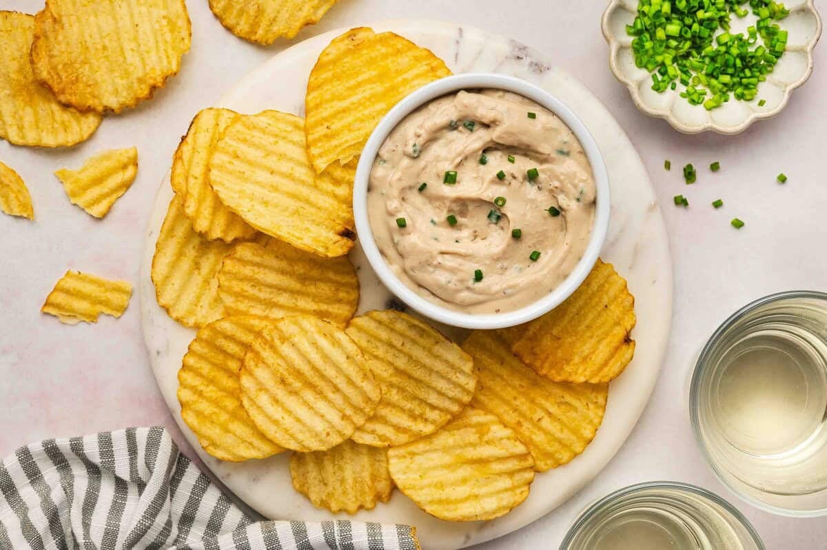 Overhead view of French onion dip garnished with chives, surrounded by crinkle-cut potato chips