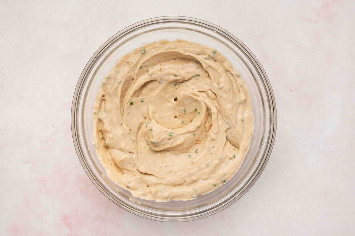 Creamy French onion dip fully mixed in a glass bowl, showing smooth texture with flecks of onion and chives